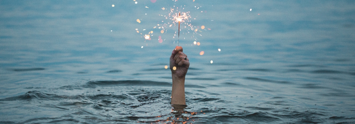 Hand mit Wunderkerze im Meer. Bild: kristopher roller 188180 unsplash