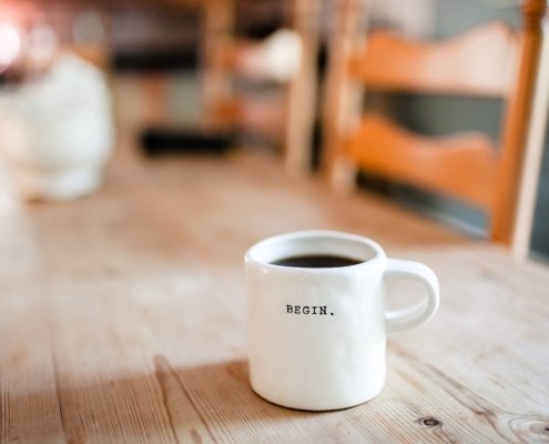 Weiße Tasse auf Holztisch, Aufschrift "begin"